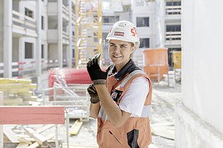 Foto Frau mit Helm auf Baustelle zieht Handschuhe an