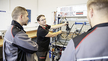 Foto Drei Männer stehen vor einer Werkbank, der hintere erklärt