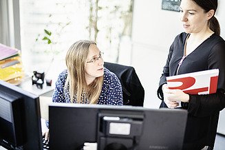 Foto: Două angajate discută în fața a două ecrane